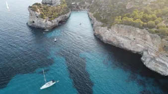 Cala de acantilados claros con el velero fondeado, vista aérea